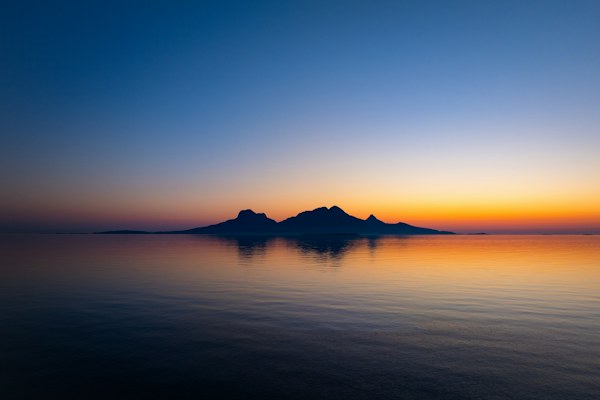 Pieni saari auringonlaskun aikaan heijastuu tyynessä merivedessä.